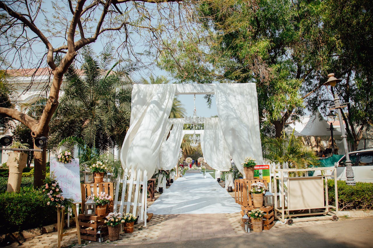 portfolio-01 Beautiful outdoor wedding archway decorated with white drapes and flowers surrounded by trees.